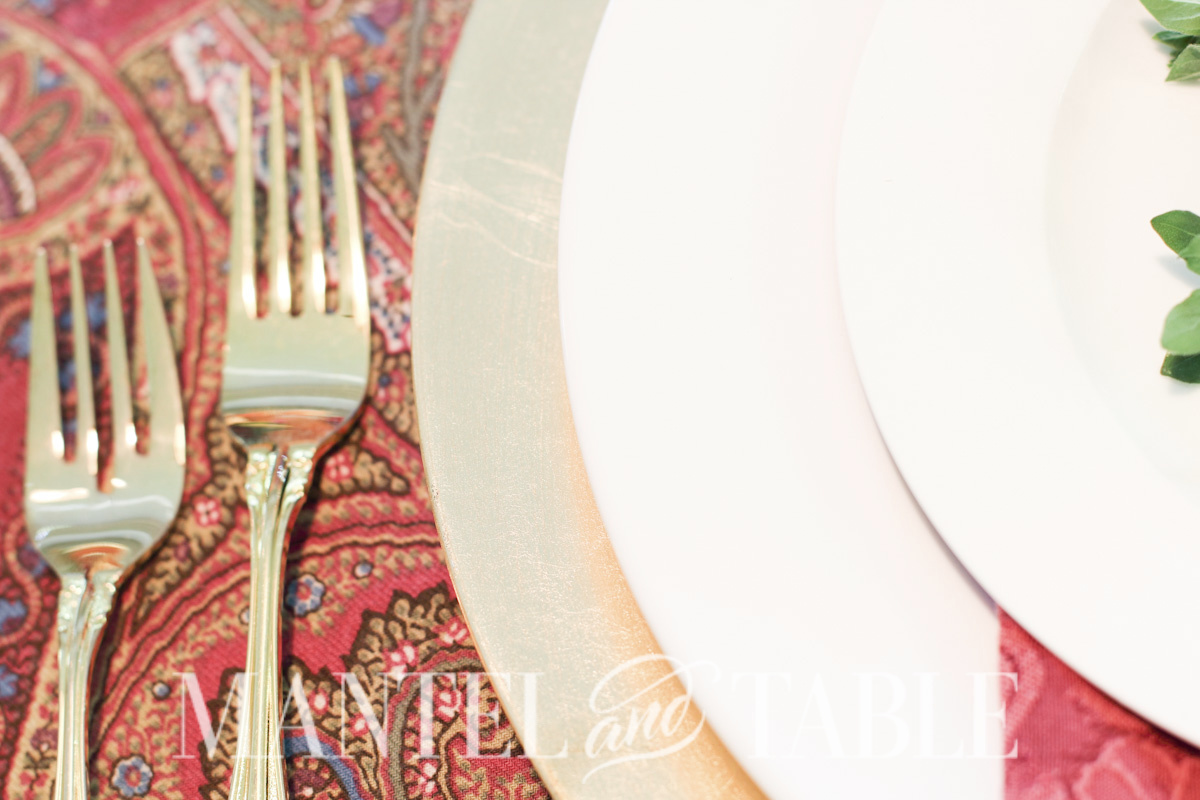 Closeup of gold forks and plate stack on red paisley tablecloth