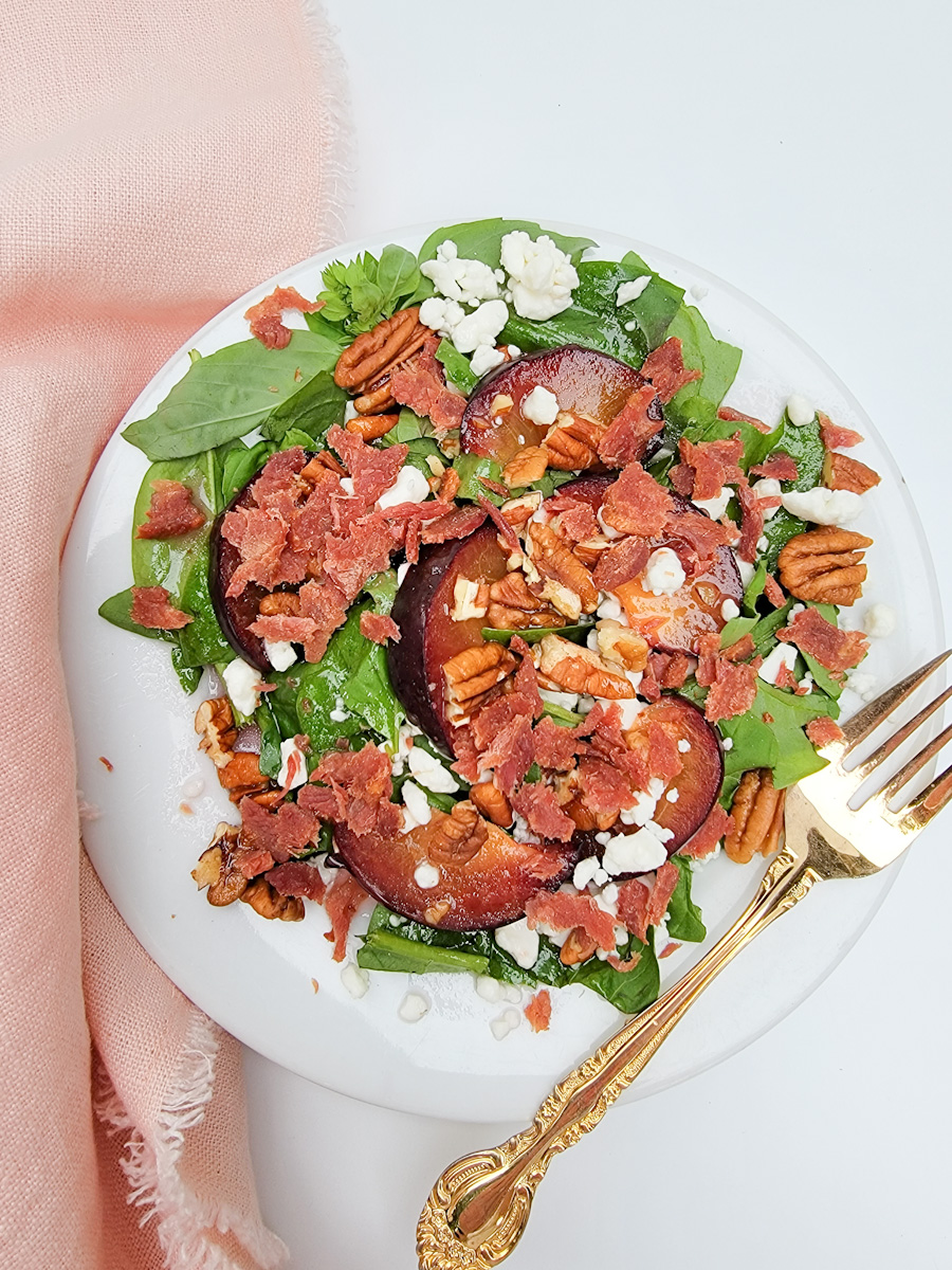 Summer Salad with plums and bacon on white plate, pink napkin