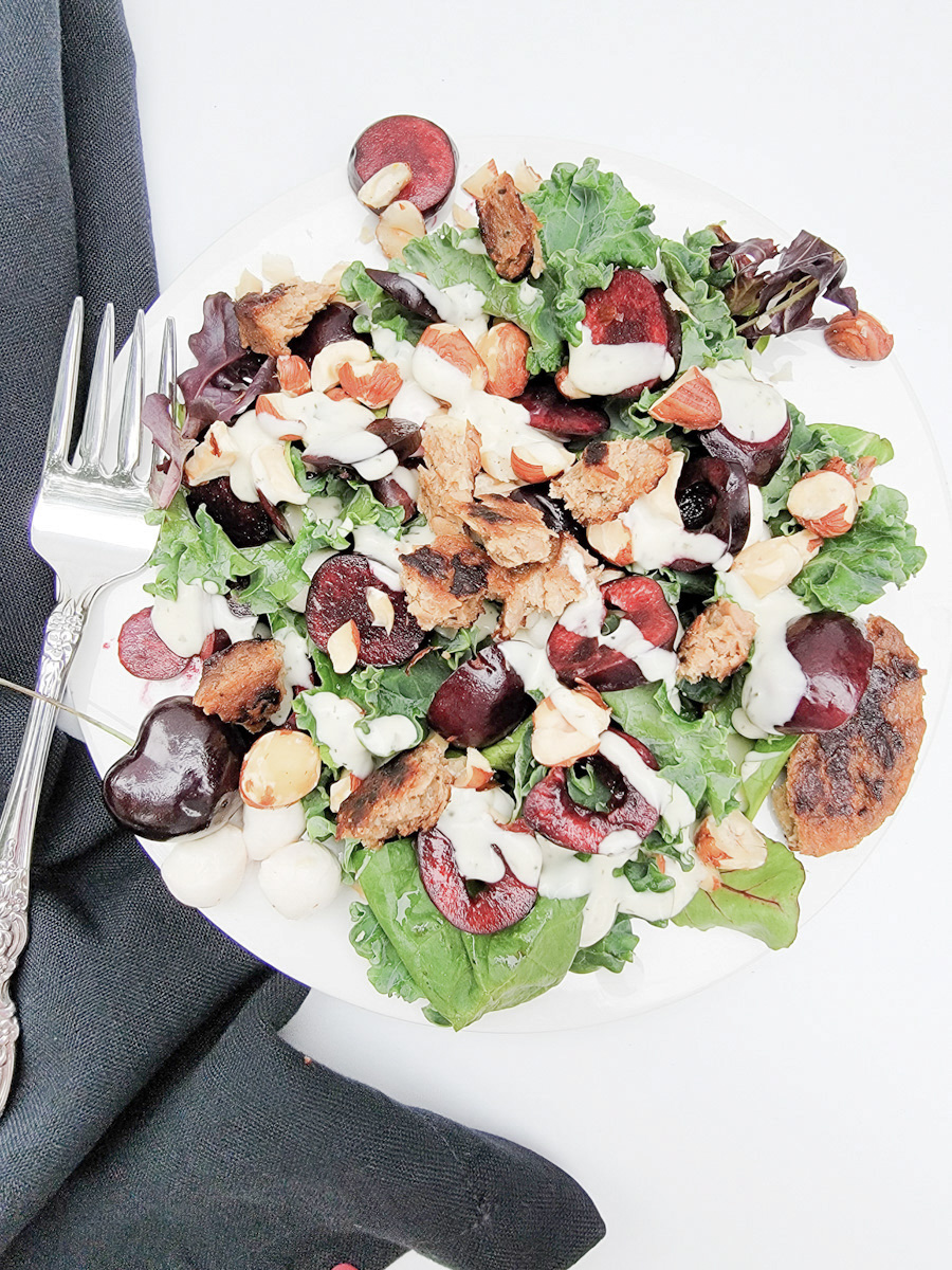 Summer Salad with cherries and garden patty on white plate, black napkin