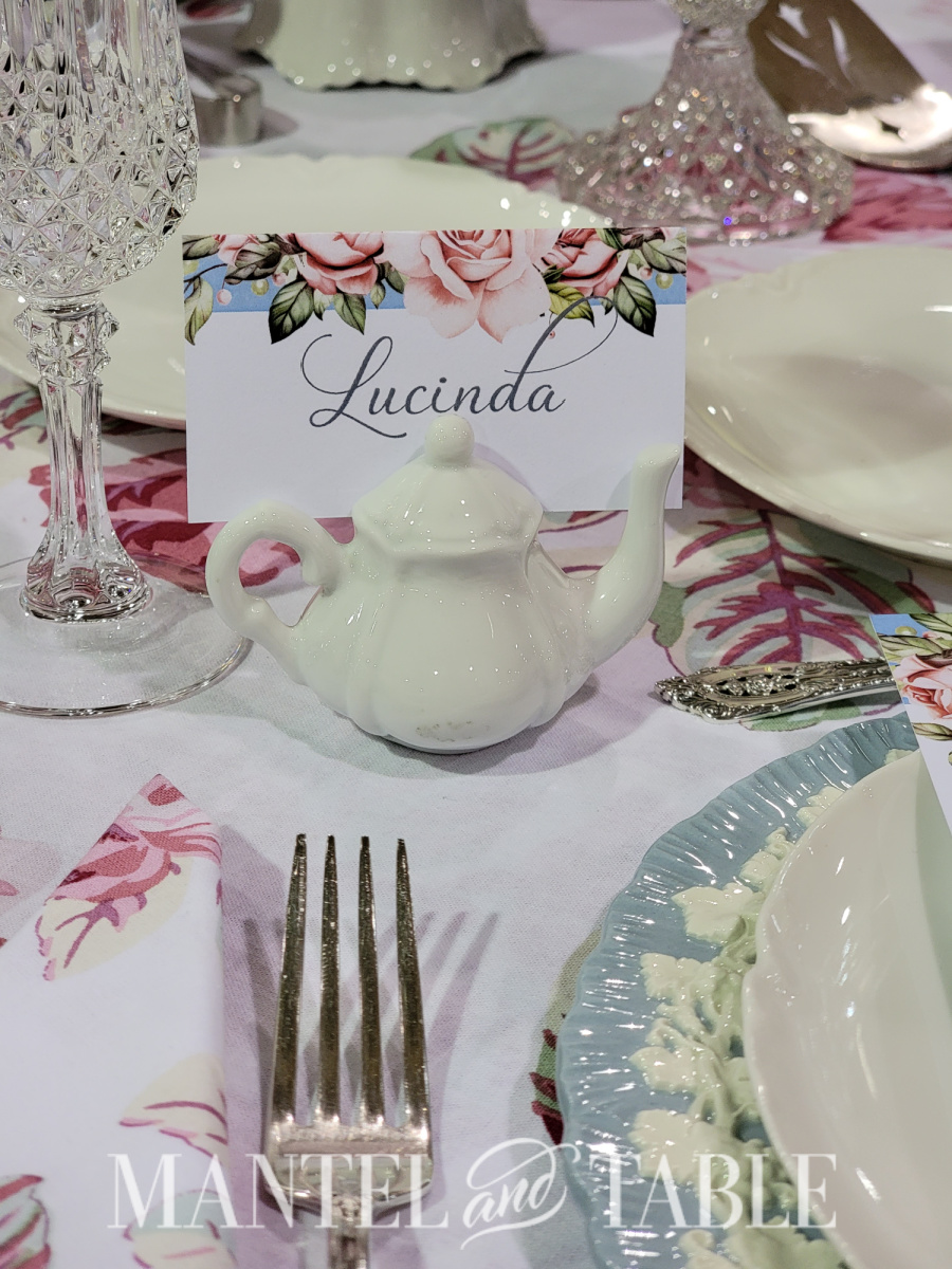Closup of place card with pink and blue flowers in a white ceramic teapot holder