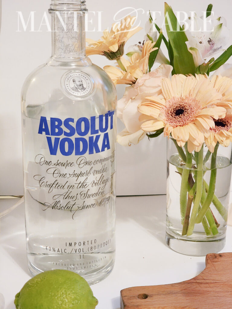 Absolut vodk,a bottle on counter with lime alight yellow flower arrangement