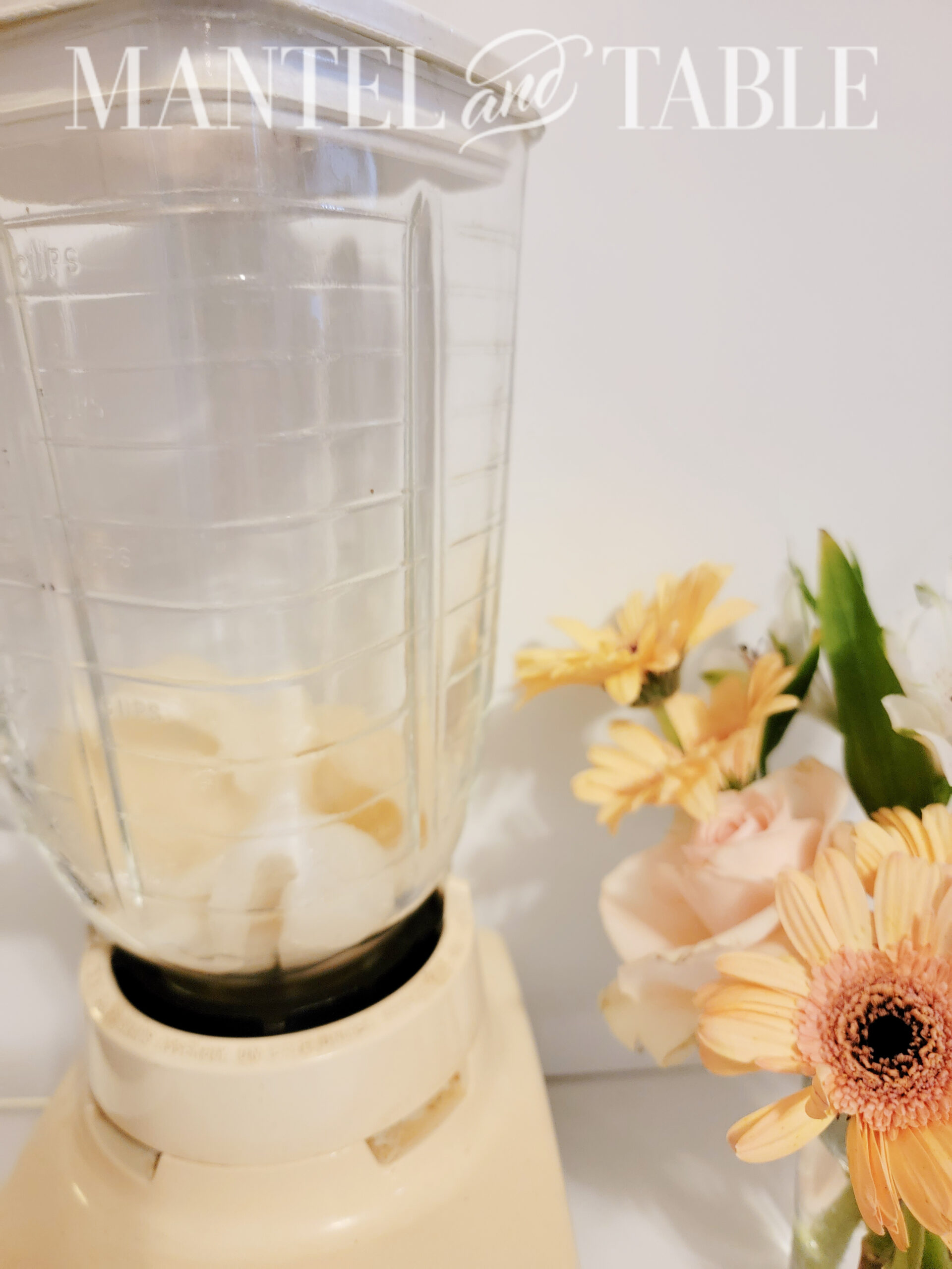 Blender with light colored melon inside on white counter with flower arrangement