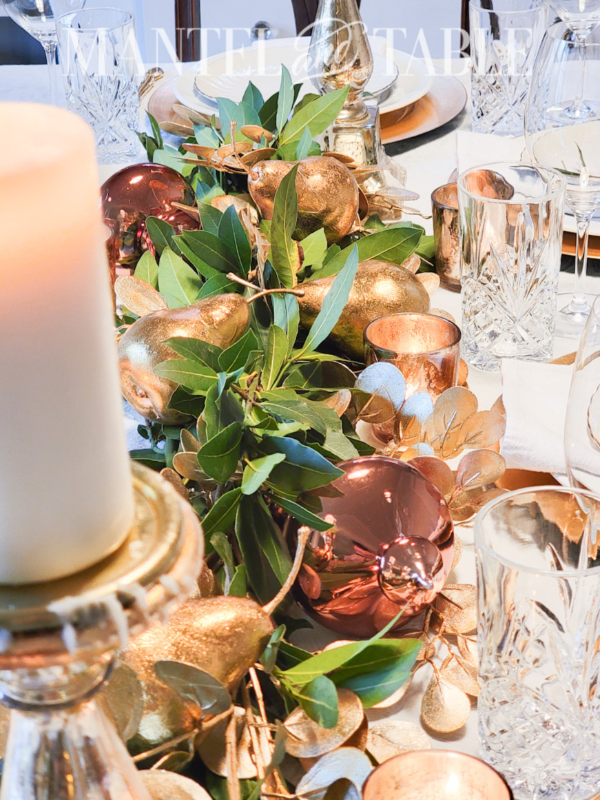 Gold and white table setting with copper colored ornaments in the bay leave garland centerpiece