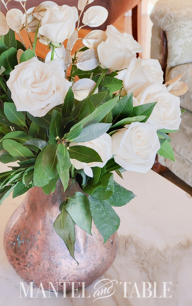 Bouquet of white roses and bay branches in copper pitcher