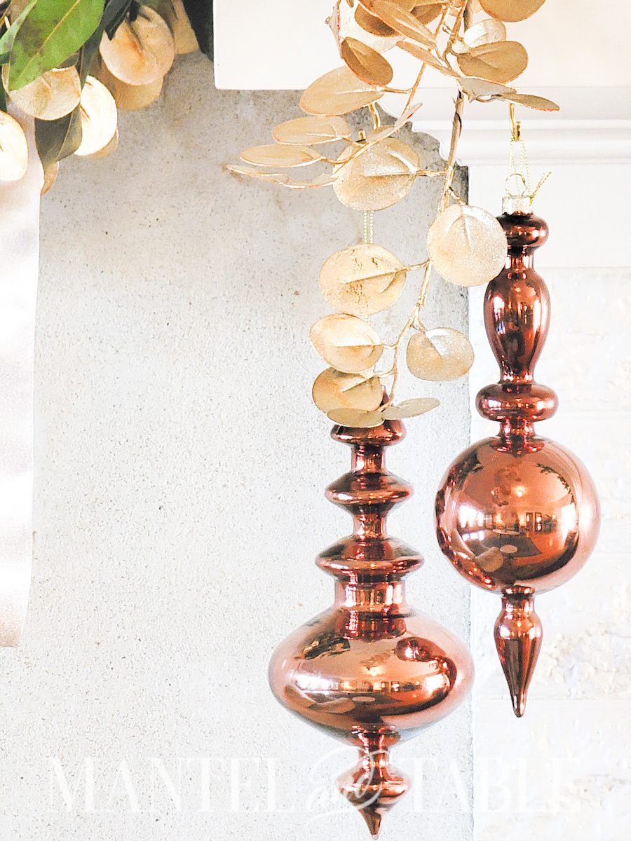 Closeup of two copper-colored glass ornaments hanging off a mantel