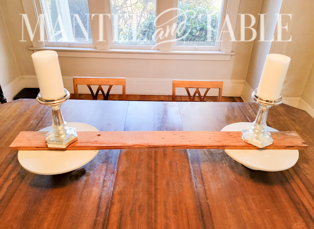 Two cake stands on a table with a board across the top and pillar candles on the board