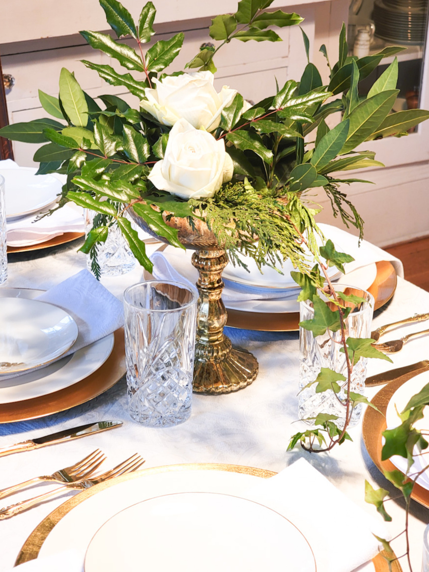 Closeup of gold vase with winter greenery and white roses on a table