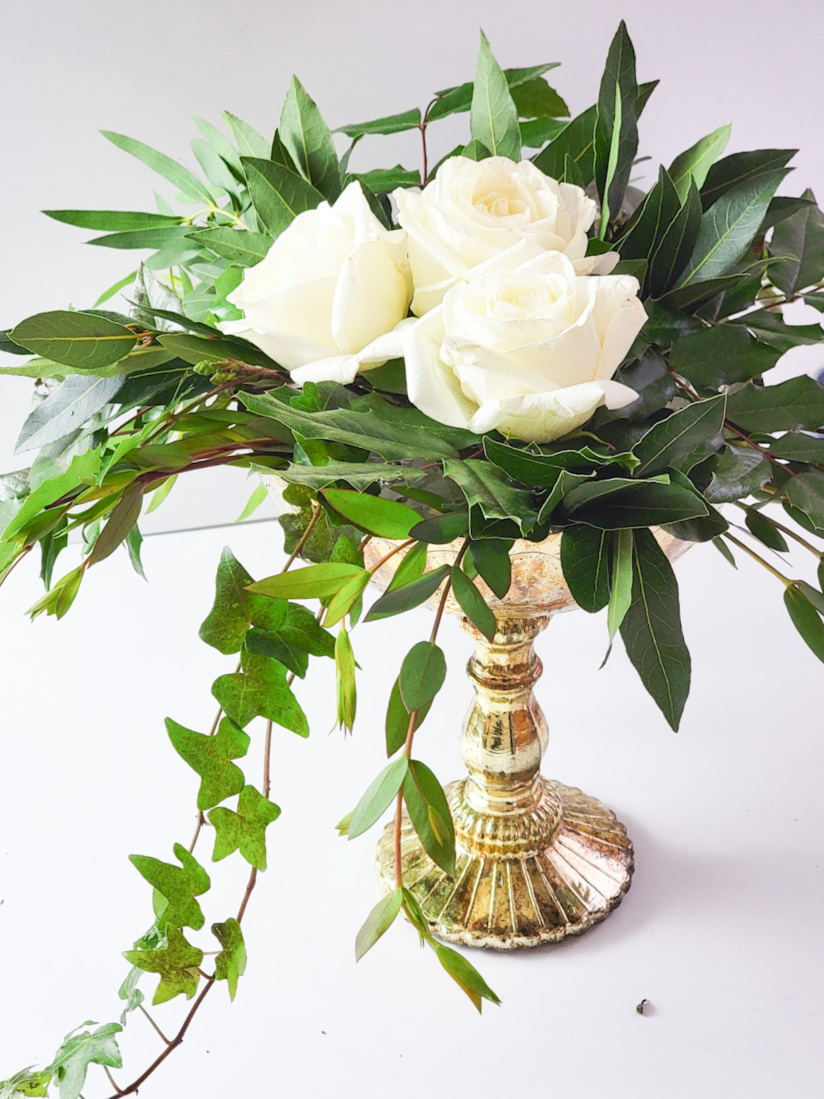 Closeup of gold vase with greenery and roses