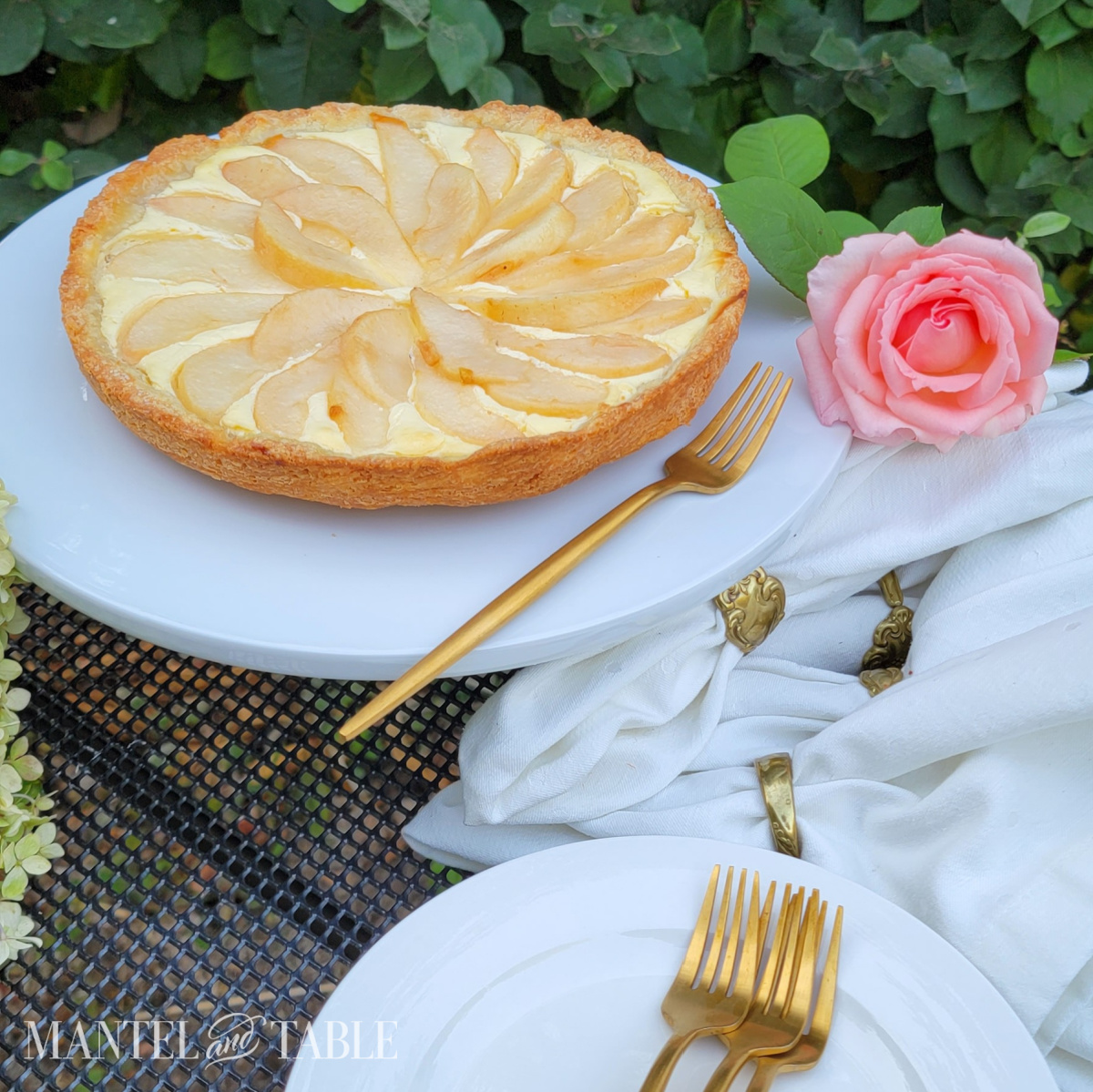 Golden pear tart on a table with a pink rose, white napkins, and gold flatware